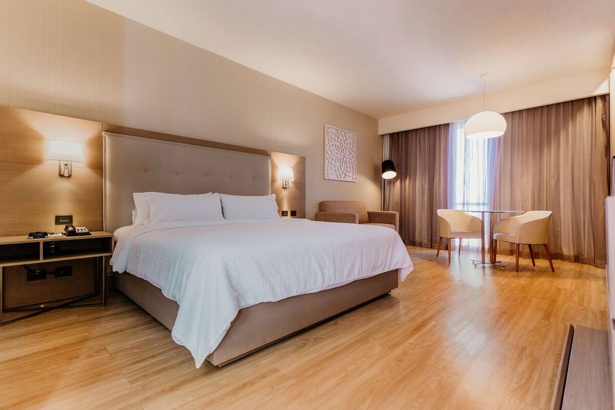 Una habitación de hotel moderna con una cama grande, mesitas de noche, un escritorio y una zona de estar con dos sillones.