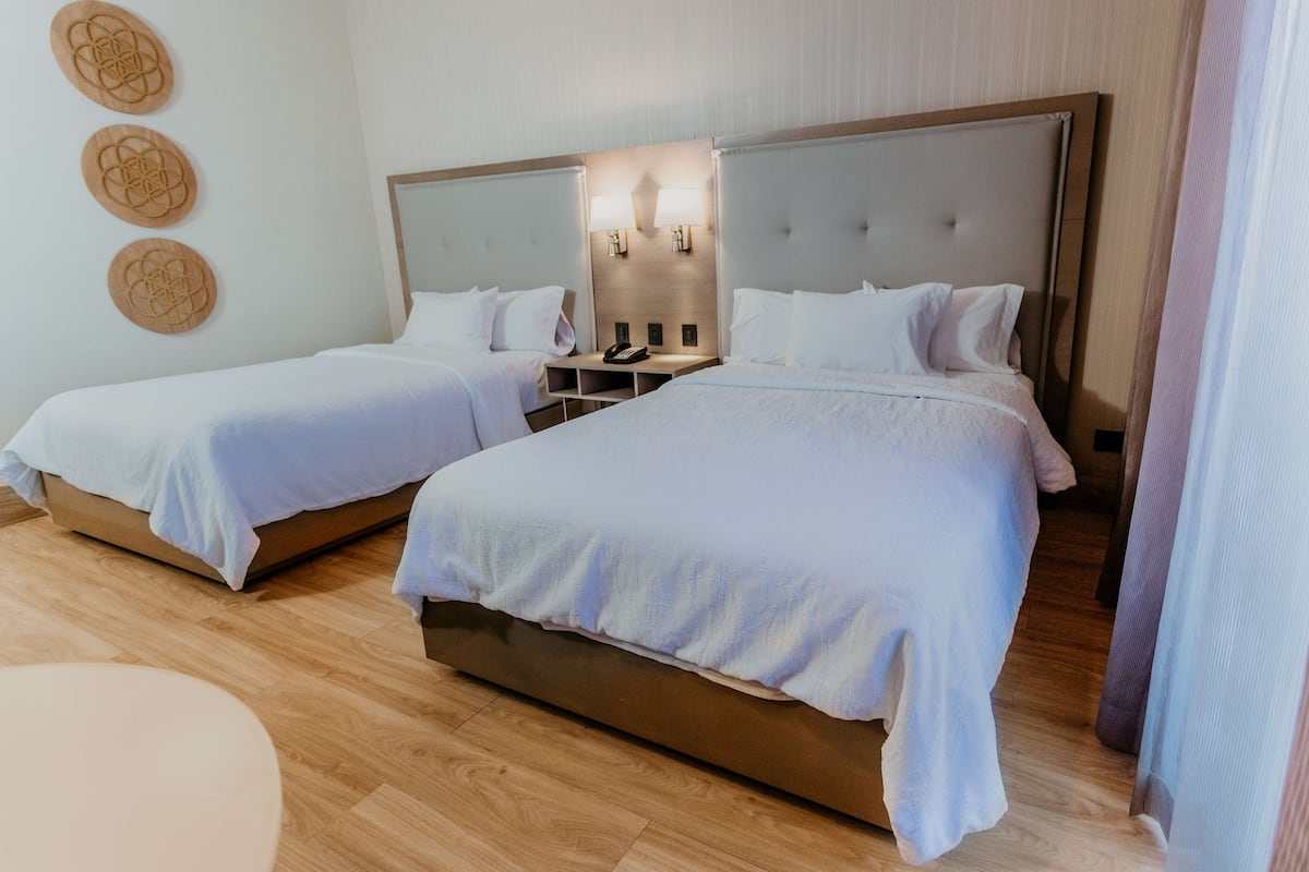 Una habitación de hotel con dos camas individuales, una mesita de noche con teléfono y lámparas fijadas a la pared.