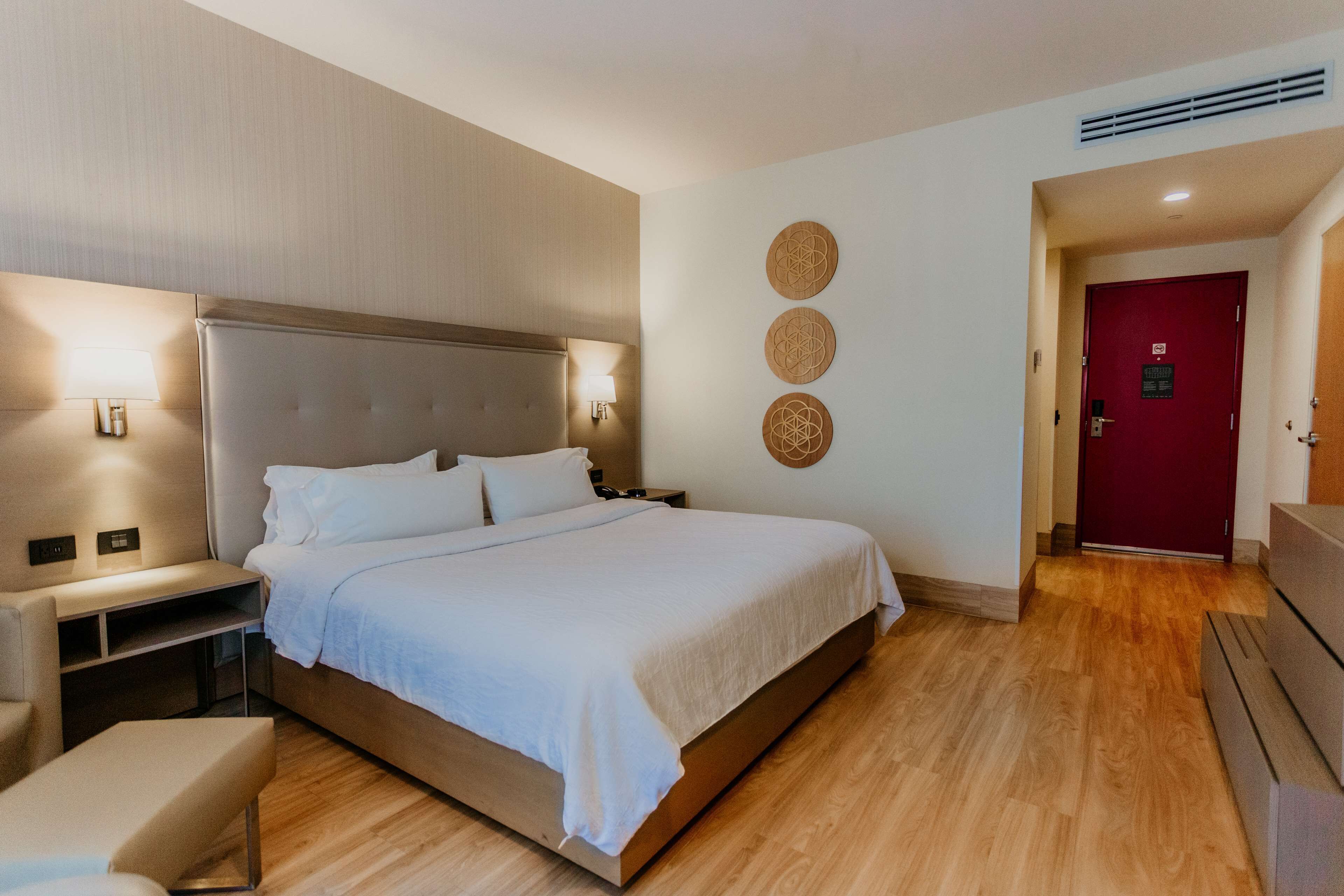A modern hotel room with a large bed, bedside tables, and a red door.