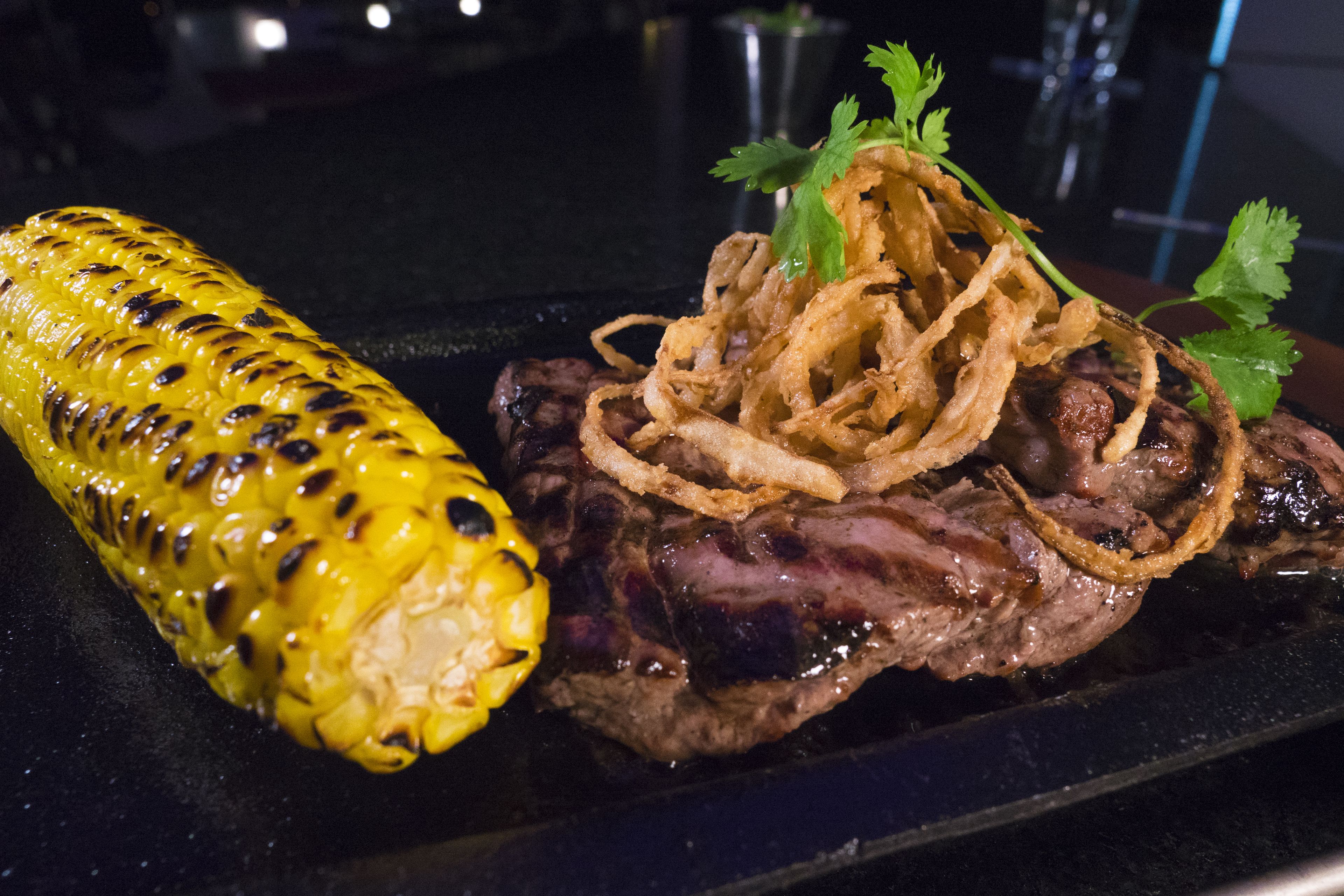 Un bistec a la parrilla con cebollas y una mazorca de maíz asada.