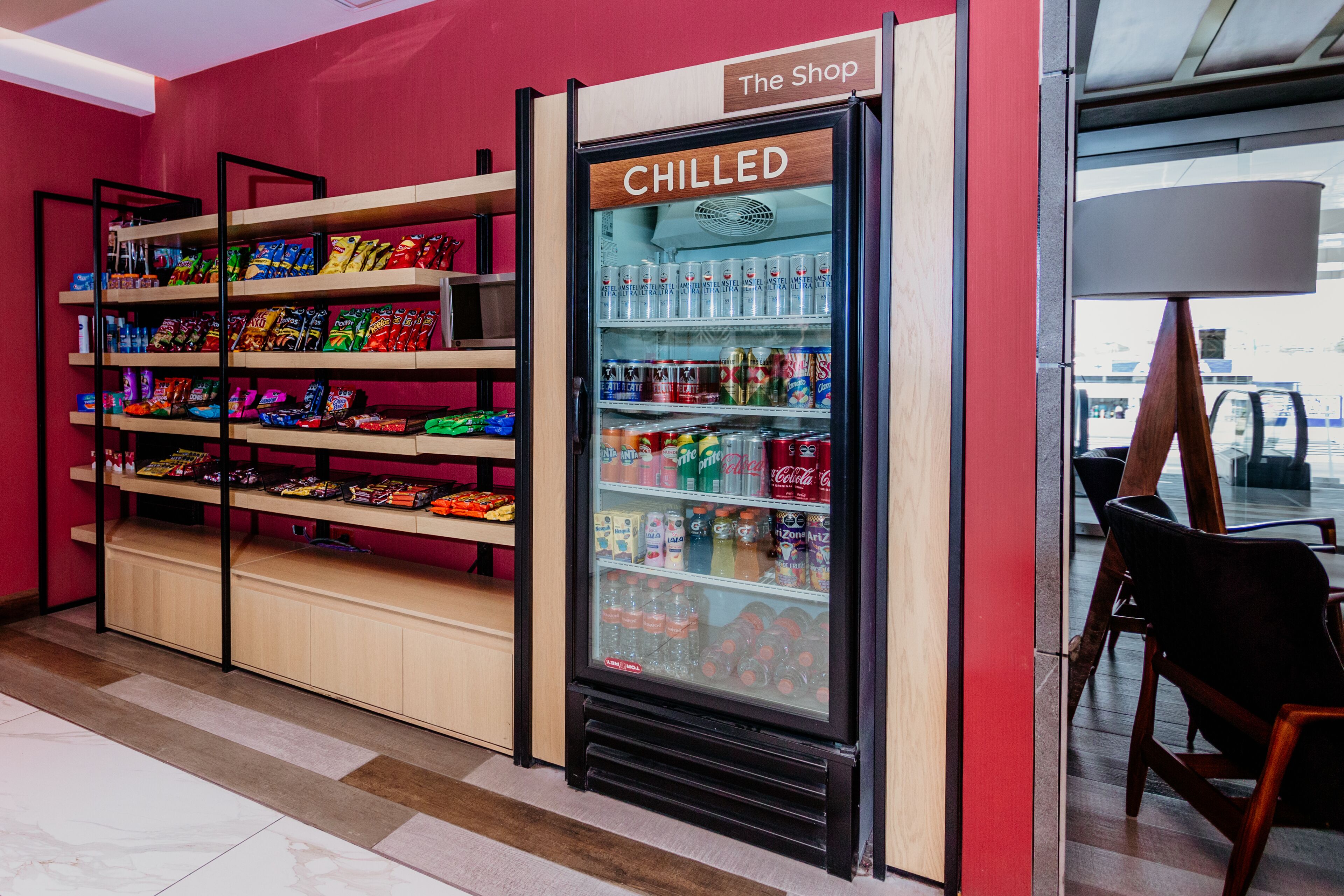 A chilled beverage display in a store with shelves of snacks and a sign reading "The Shop".