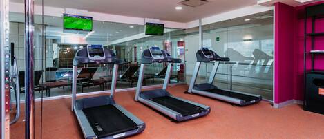 Un gimnasio con cintas de correr, una pantalla de televisión y una pared rosa.