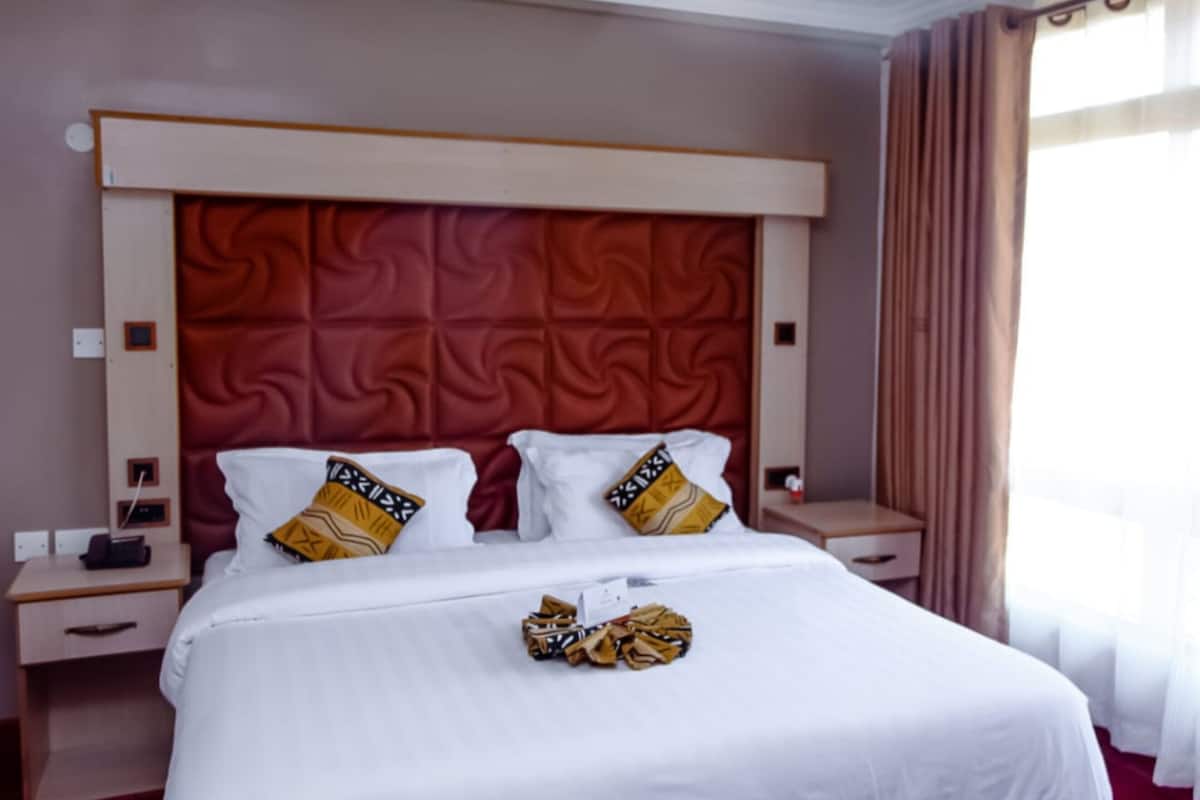 A hotel room with a large bed, two bedside tables, a red headboard, and a window with curtains.