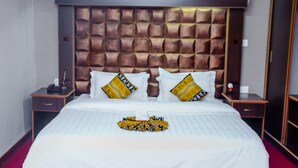 A hotel room with a large bed, a padded headboard, two bedside tables, and a red carpet.