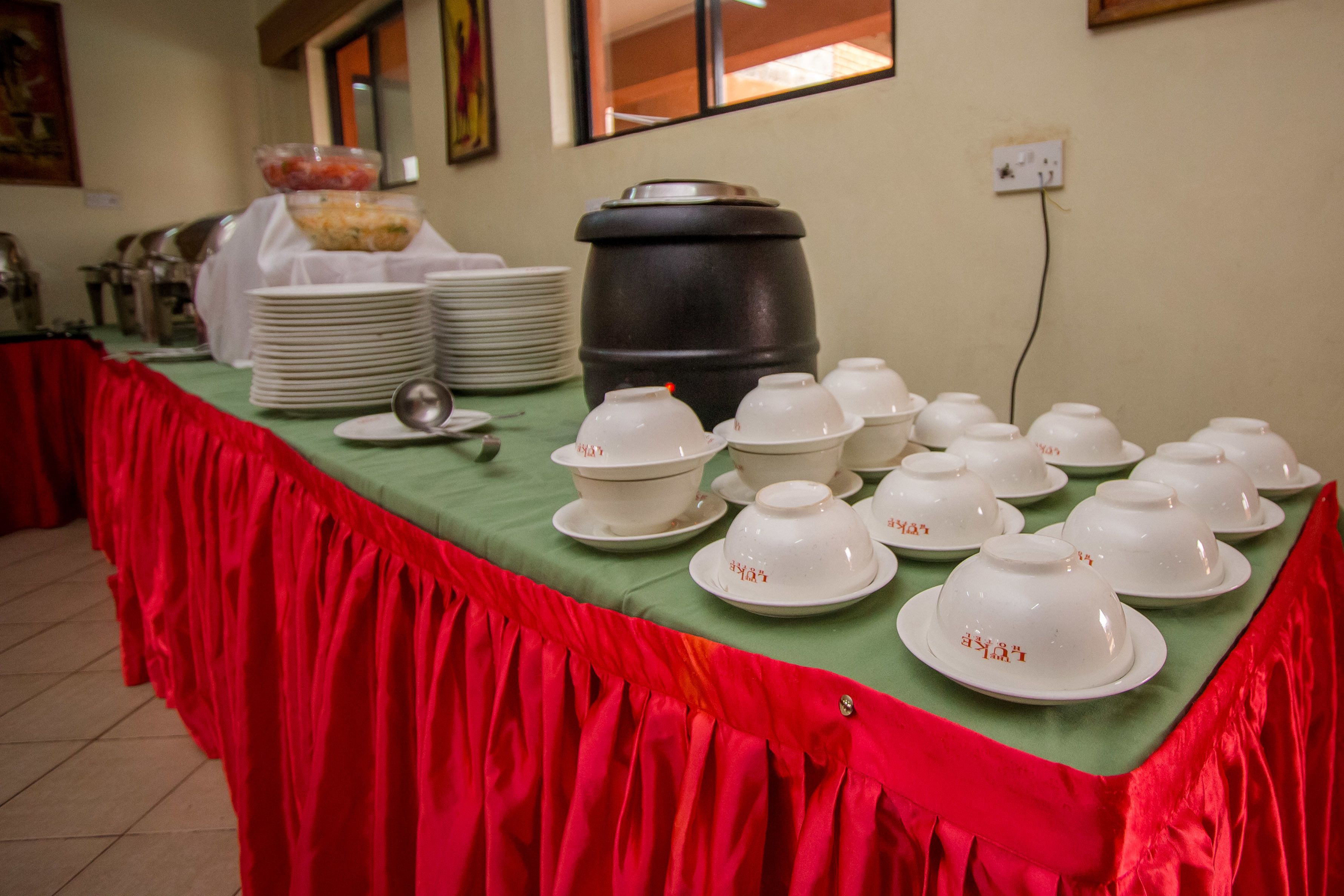 Une table de buffet avec des bols et des assiettes blancs, un grand récipient noir et une nappe rouge.