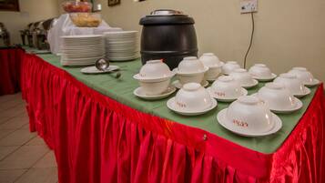 Une table de buffet avec des bols et des assiettes blancs, un grand récipient noir et une nappe rouge.
