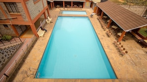 A rectangular pool with a tiled deck, surrounded by outdoor seating and a covered area with tables and chairs.