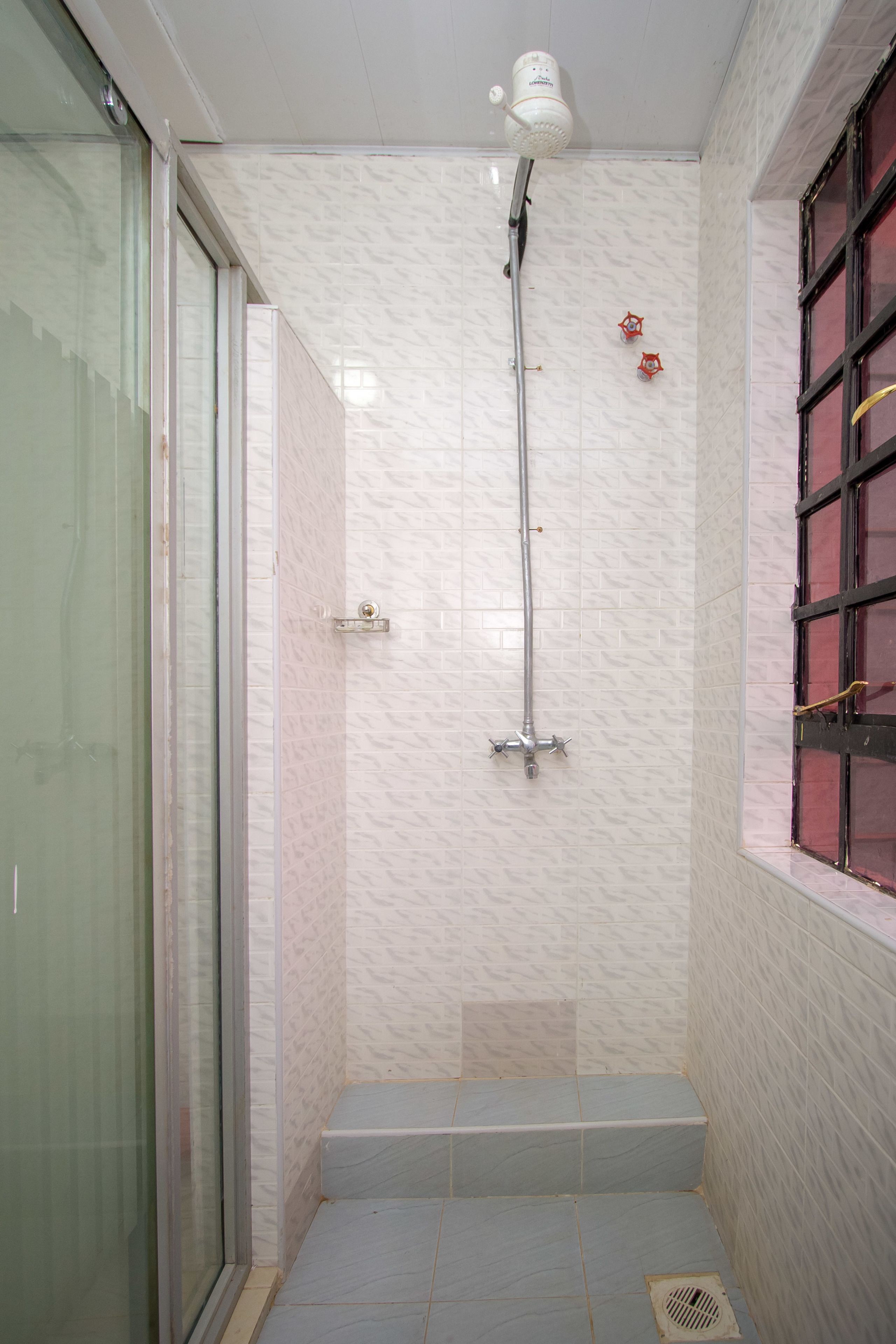 A shower area with a glass door, a tiled wall, and a window with red-tinted glass.