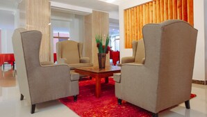 A hotel lobby with two armchairs, a wooden coffee table, and a red carpet.