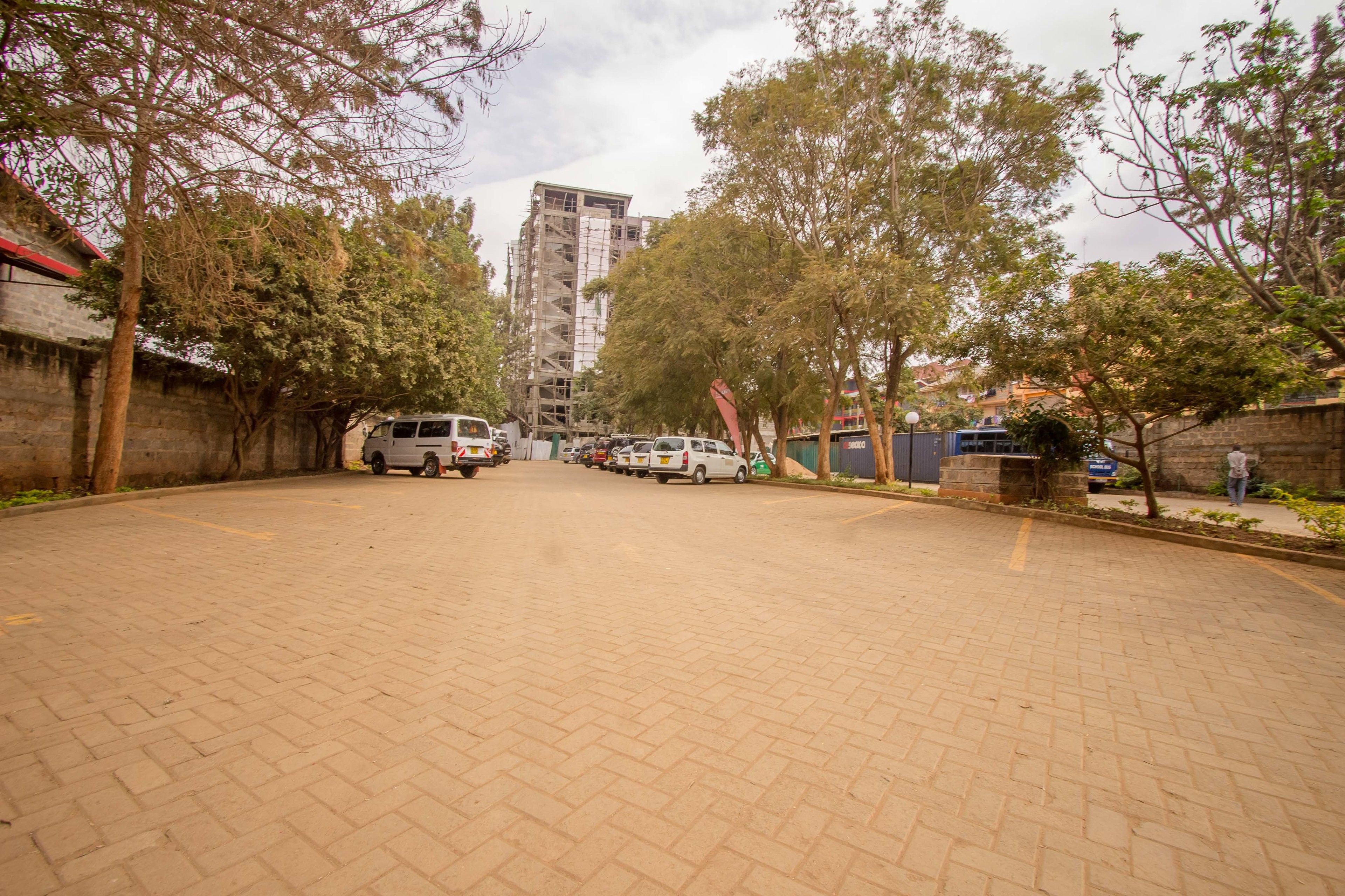 A paved courtyard with parked vehicles and trees.
