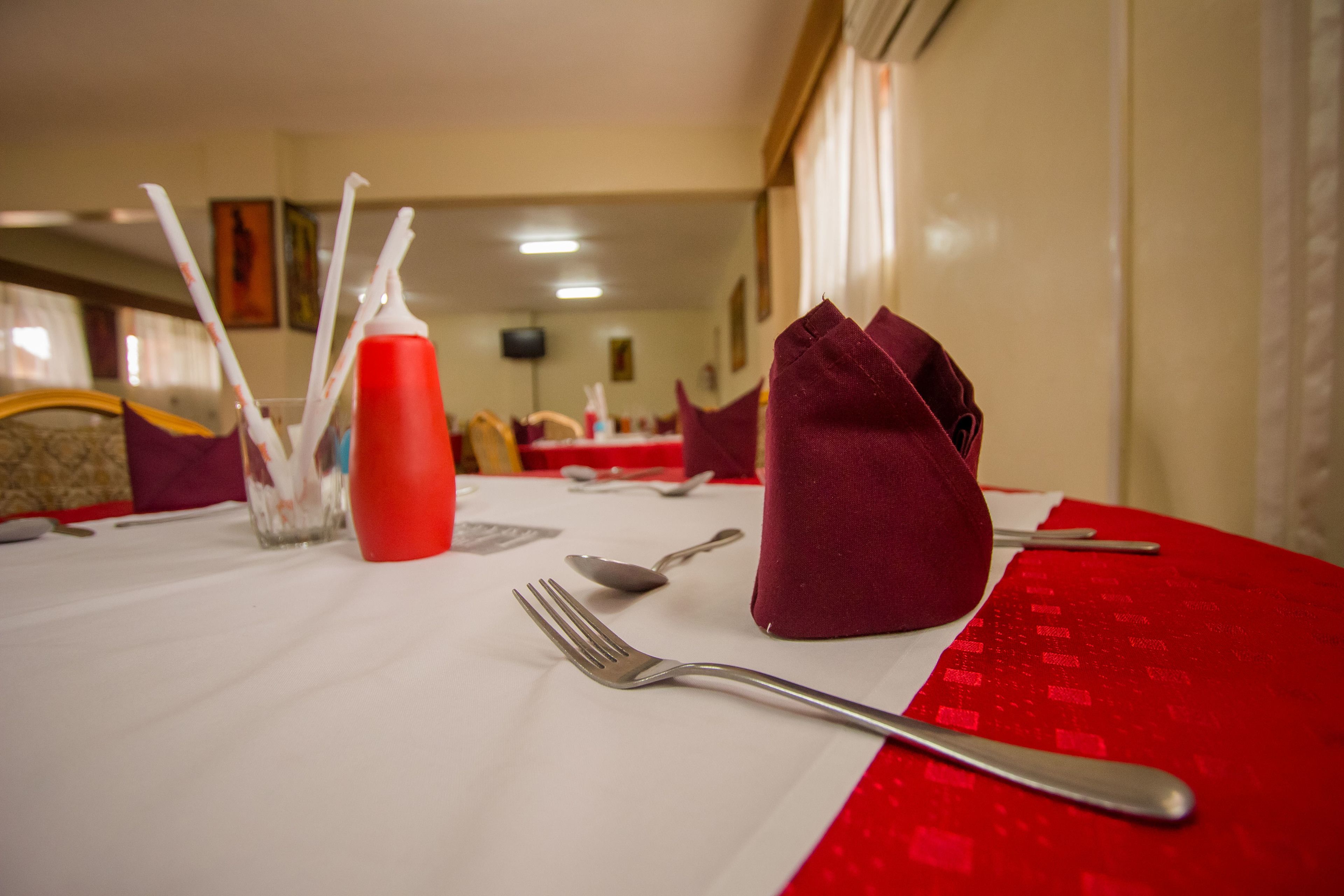 Una mesa de comedor dispuesta con cubiertos, una servilleta roja y un vaso con pajitas.