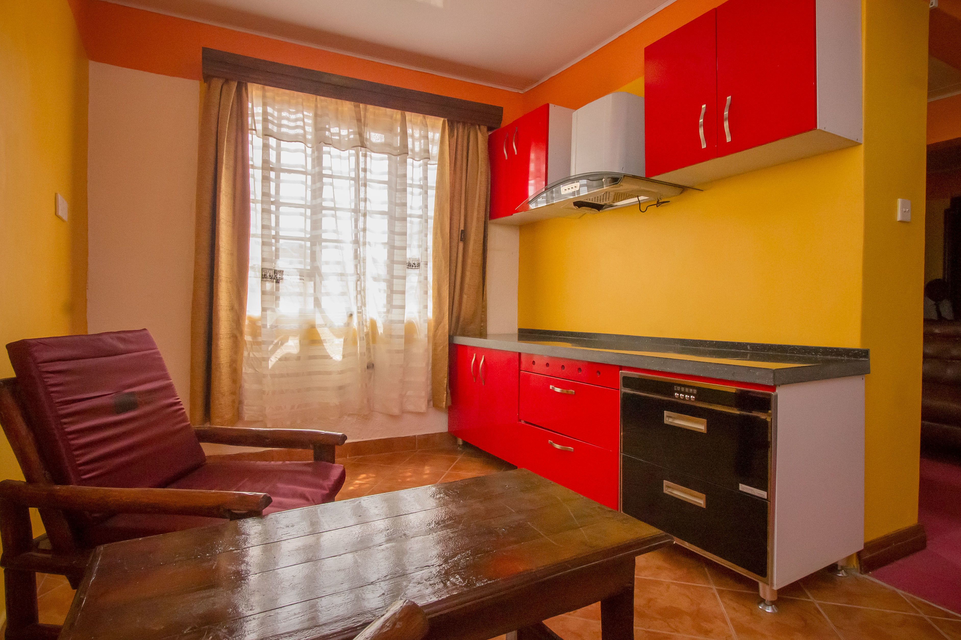 A compact kitchen with red cabinets, a black countertop, and a wooden table.