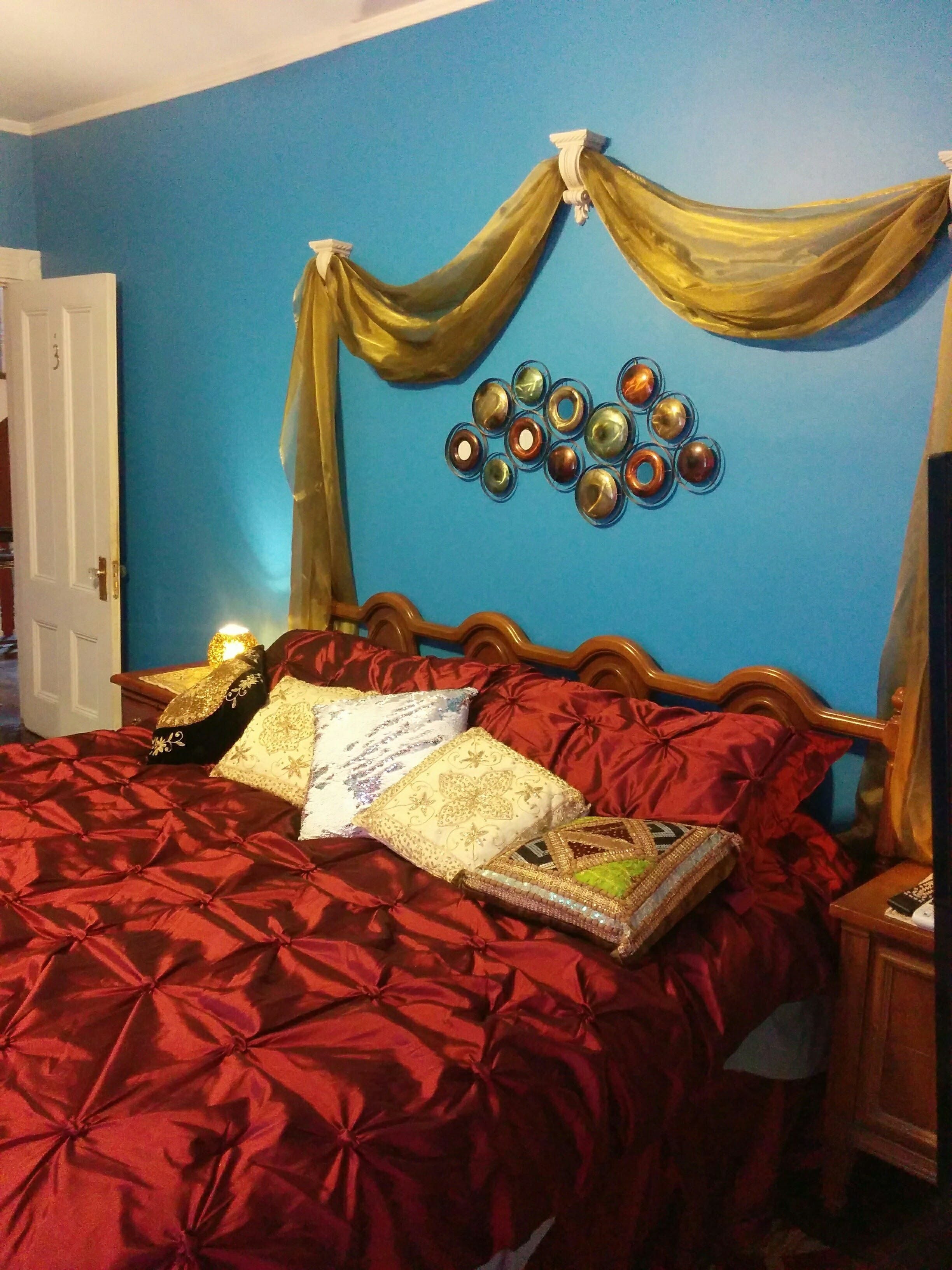 A bed with red bedding, a decorative pillow, and a wall art piece.