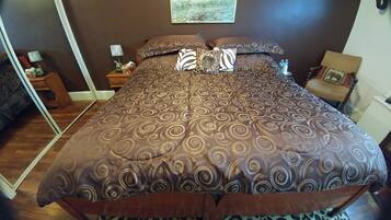 Un dormitorio con una cama grande, ropa de cama estampada, una mesita de noche con una lámpara y un cuadro en la pared.