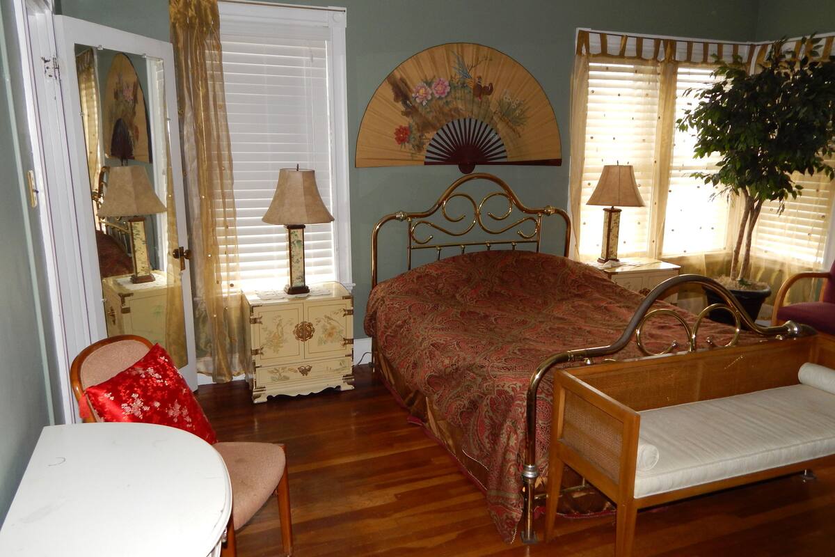Une chambre à coucher avec un lit en bois, deux tables de chevet avec des lampes, une chaise, une commode et un grand miroir.