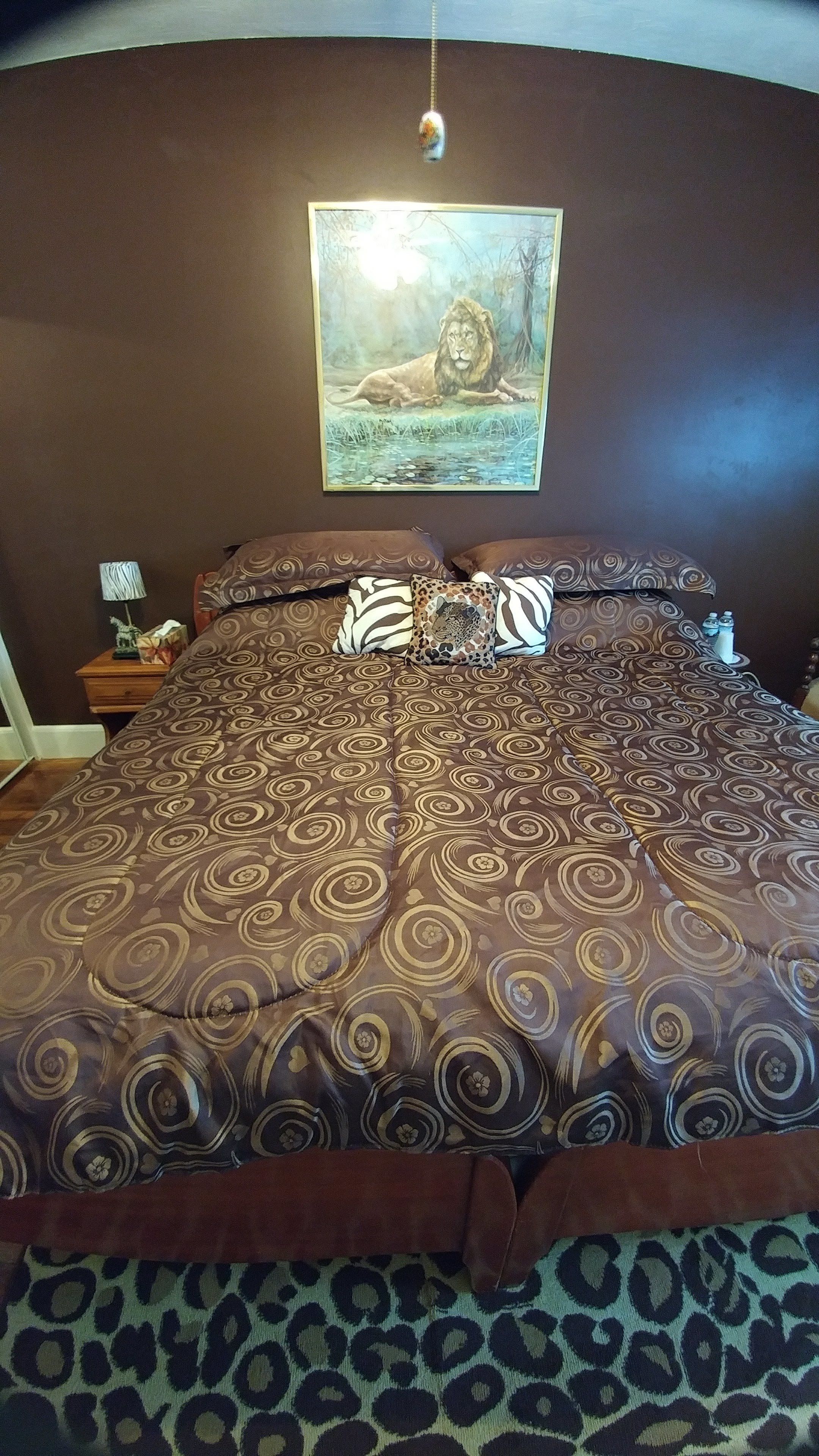 A bedroom with a large bed, patterned bedding, a painting of a lion, and a leopard print rug.