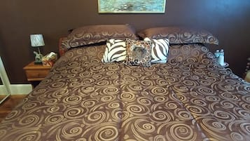 A bedroom with a large bed, patterned bedding, a painting of a lion, and a leopard print rug.