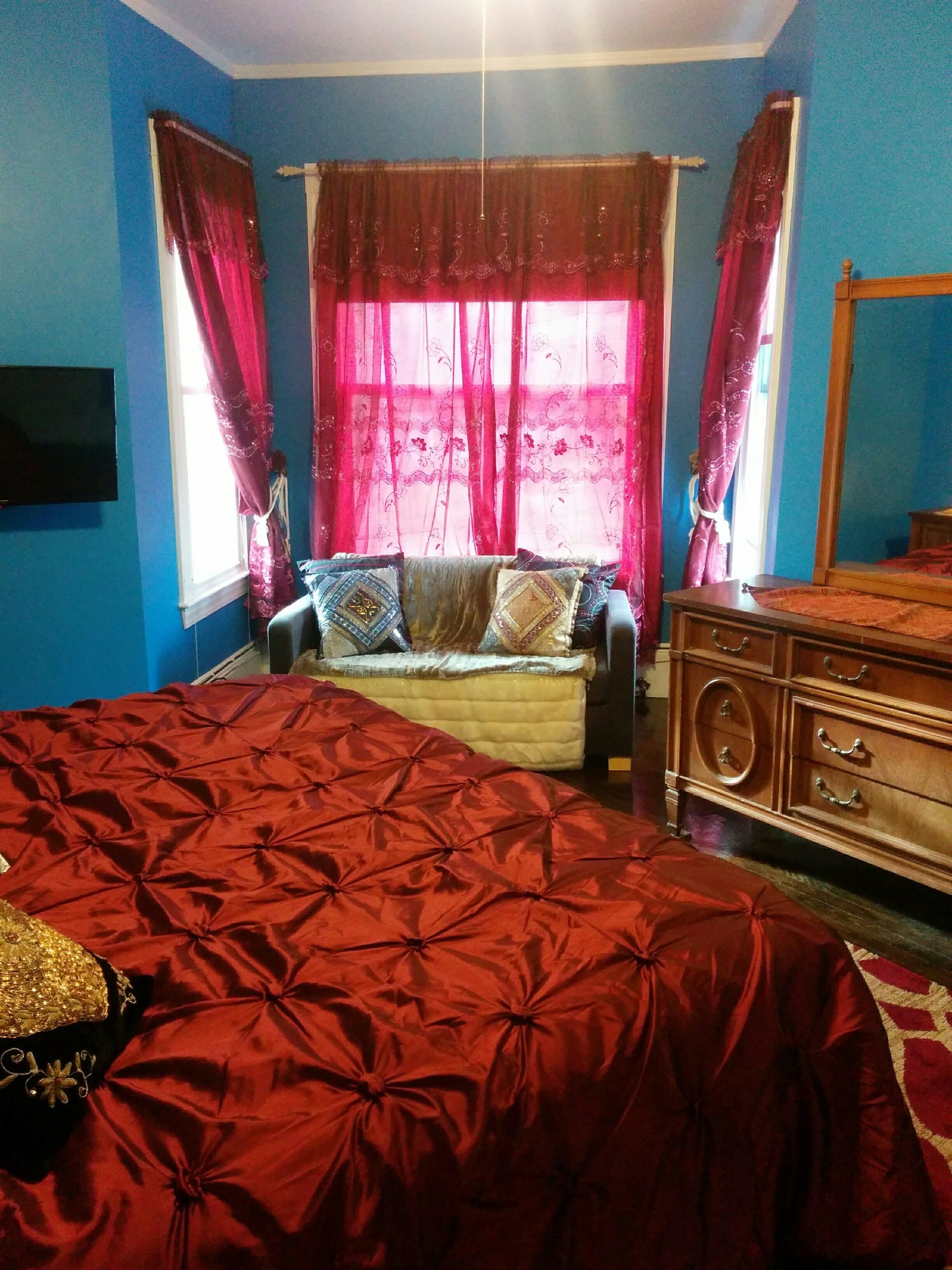 A bedroom with a large bed, a wooden dresser, and a TV mounted on the wall.