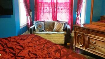 A bedroom with a large bed, a wooden dresser, and a TV mounted on the wall.