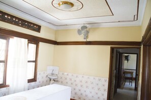 Un baño con lavamanos blanco, un ventilador y una ventana con cortinas.