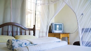 A bed with a canopy, a wooden nightstand with a television, and a window with curtains. - Keba Inn (Entebbe)