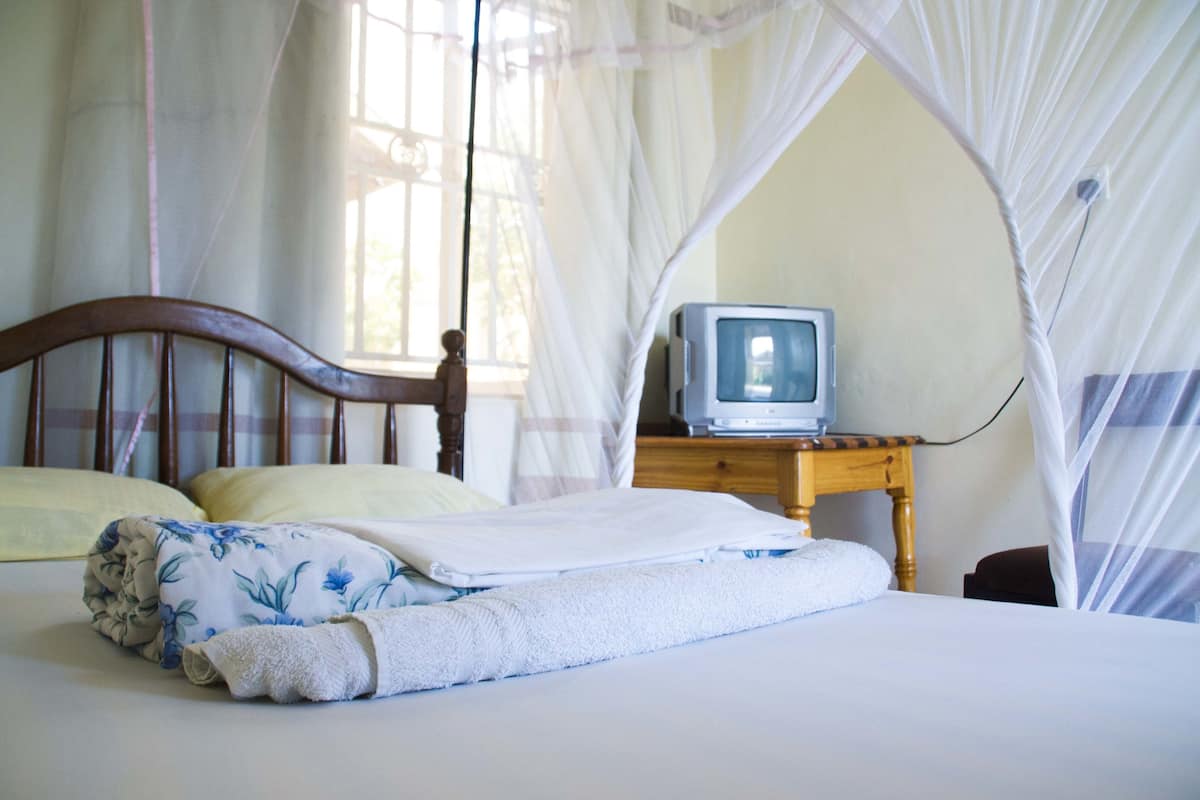 Una cama con dosel, una mesita de noche de madera con televisor y una ventana con cortinas.