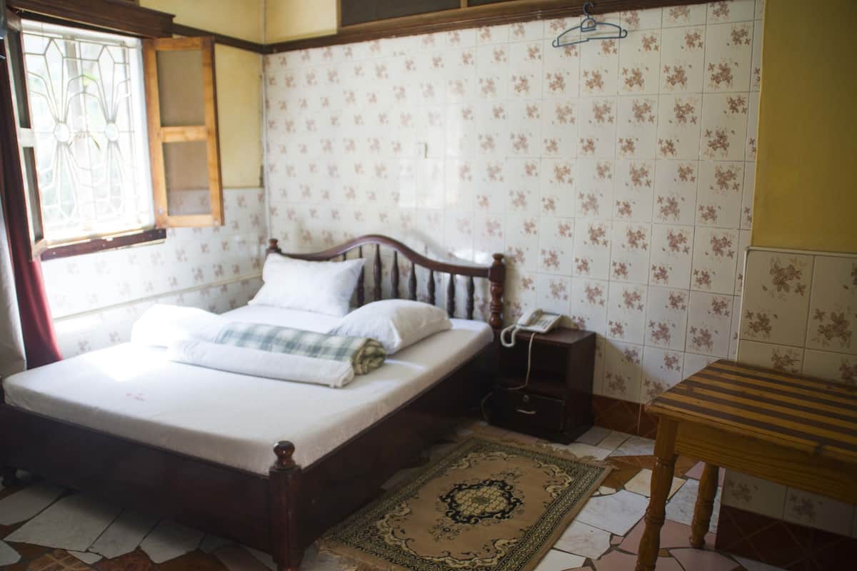 Un dormitorio con una cama de madera, un teléfono en la mesita de noche, una pequeña mesa de madera y una alfombra estampada.