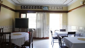 A dining area with two round tables, chairs, a television, and a window with curtains. - Keba Inn (Entebbe)