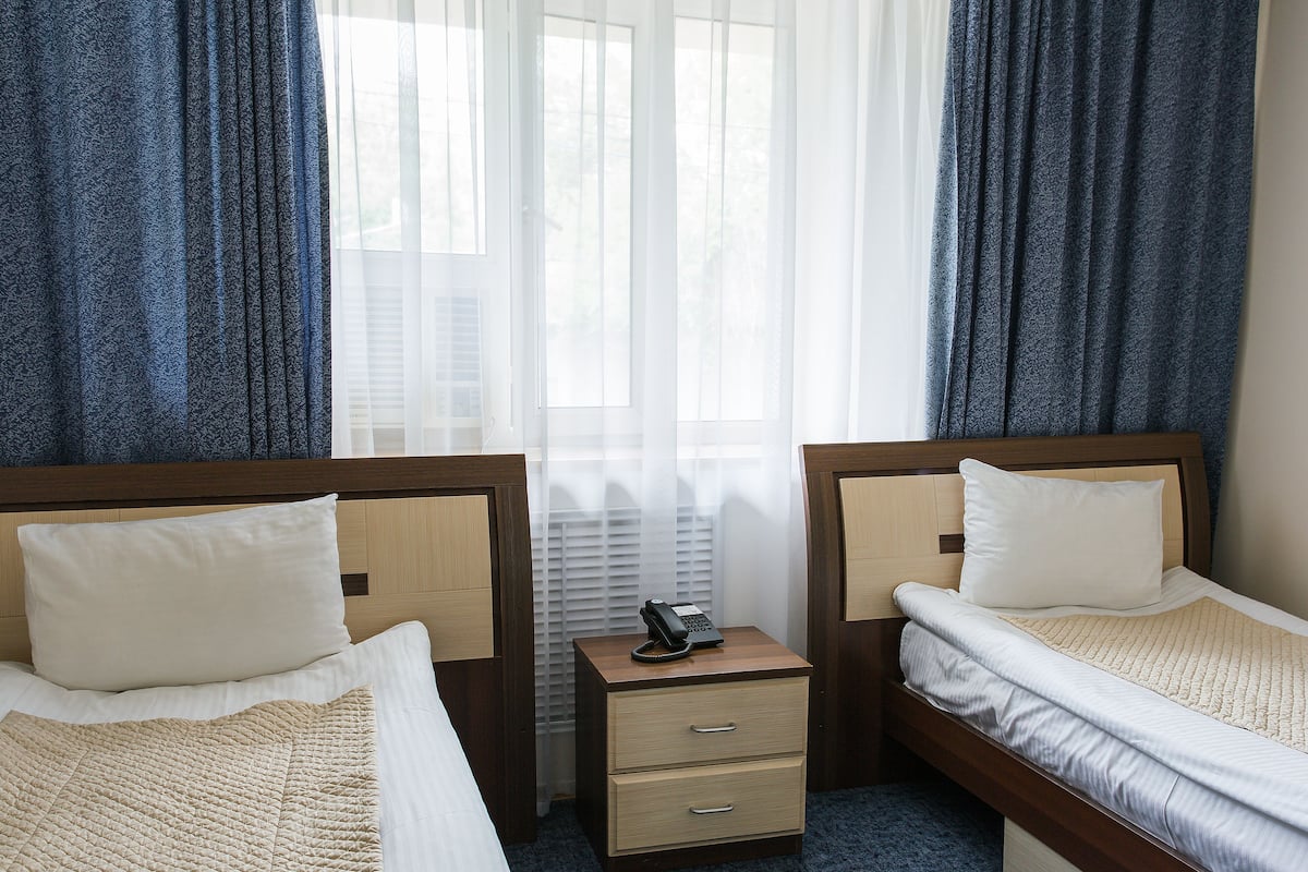 A hotel room with two single beds, a bedside table with a telephone, and a window with curtains.