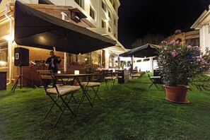 An outdoor dining area with tables and chairs, a stage with a performer, and a potted plant. - Hotel Alma (Almaty)