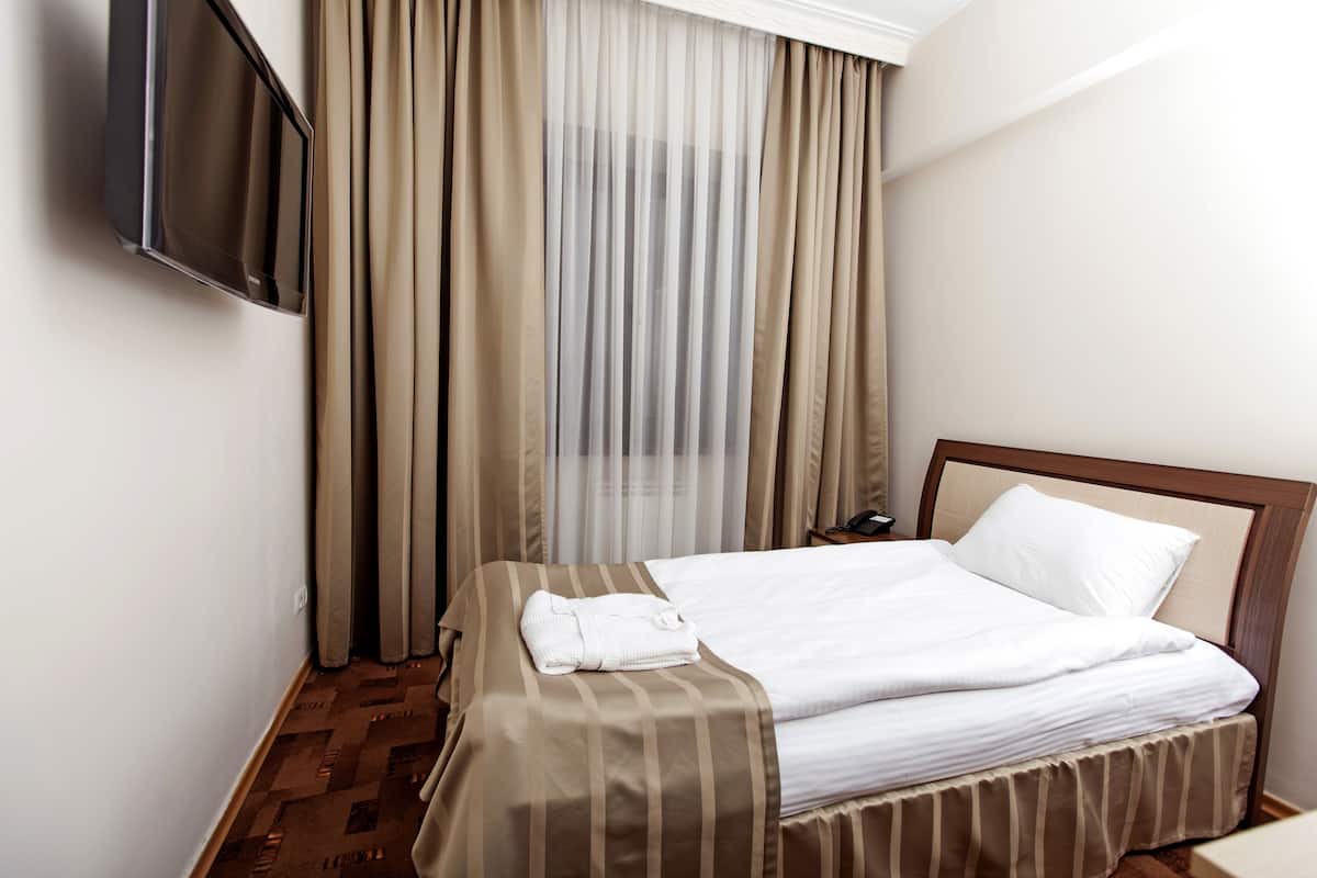 A hotel room with a bed, a TV mounted on the wall, and a window with curtains.