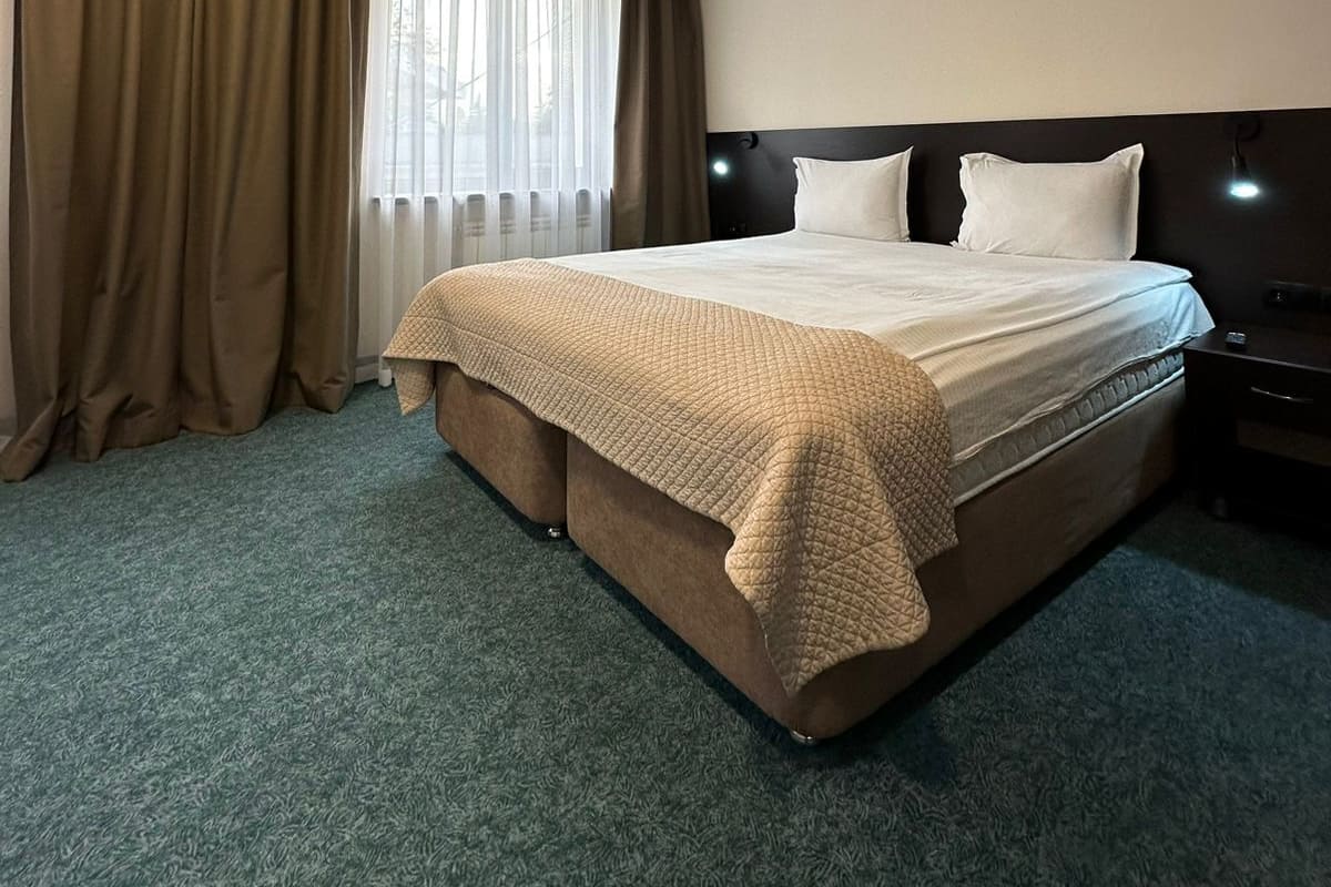 A hotel room with a large bed, a nightstand, a lamp, and a window with curtains.