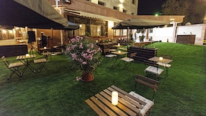 Une terrasse extérieure avec des tables et des chaises, une plante en pot et un bâtiment en arrière-plan.
