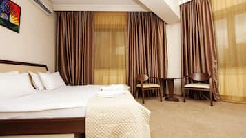 A hotel room with a bed, a chair, a table, and curtains.