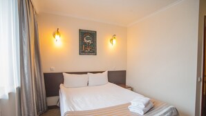 Une chambre d’hôtel avec un lit, deux appliques murales, un tableau encadré et une fenêtre avec des rideaux.