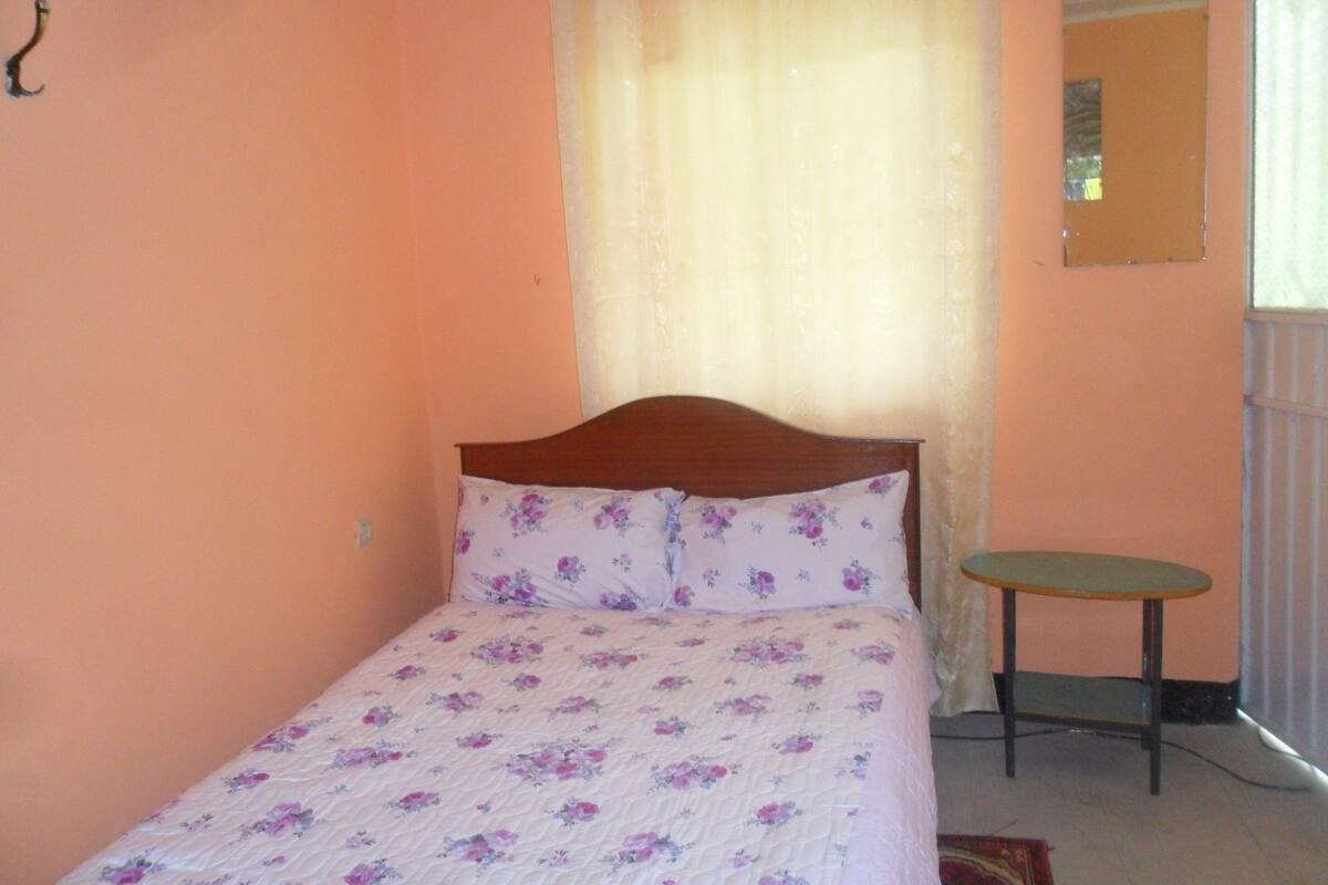 A single bed with floral bedding, a small bedside table, and a mirror on the wall.