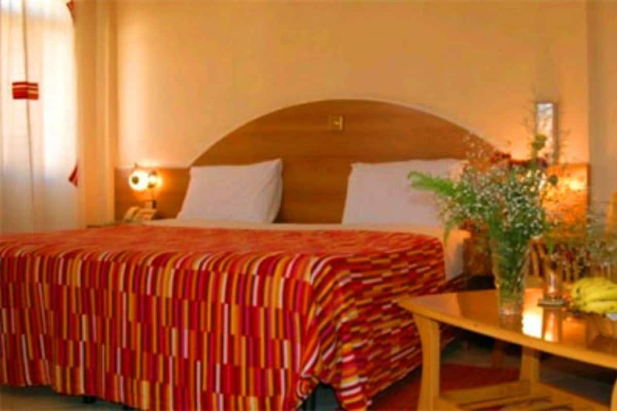 A hotel room with a large bed, a wooden headboard, a bedside table with a lamp, and a vase with flowers.