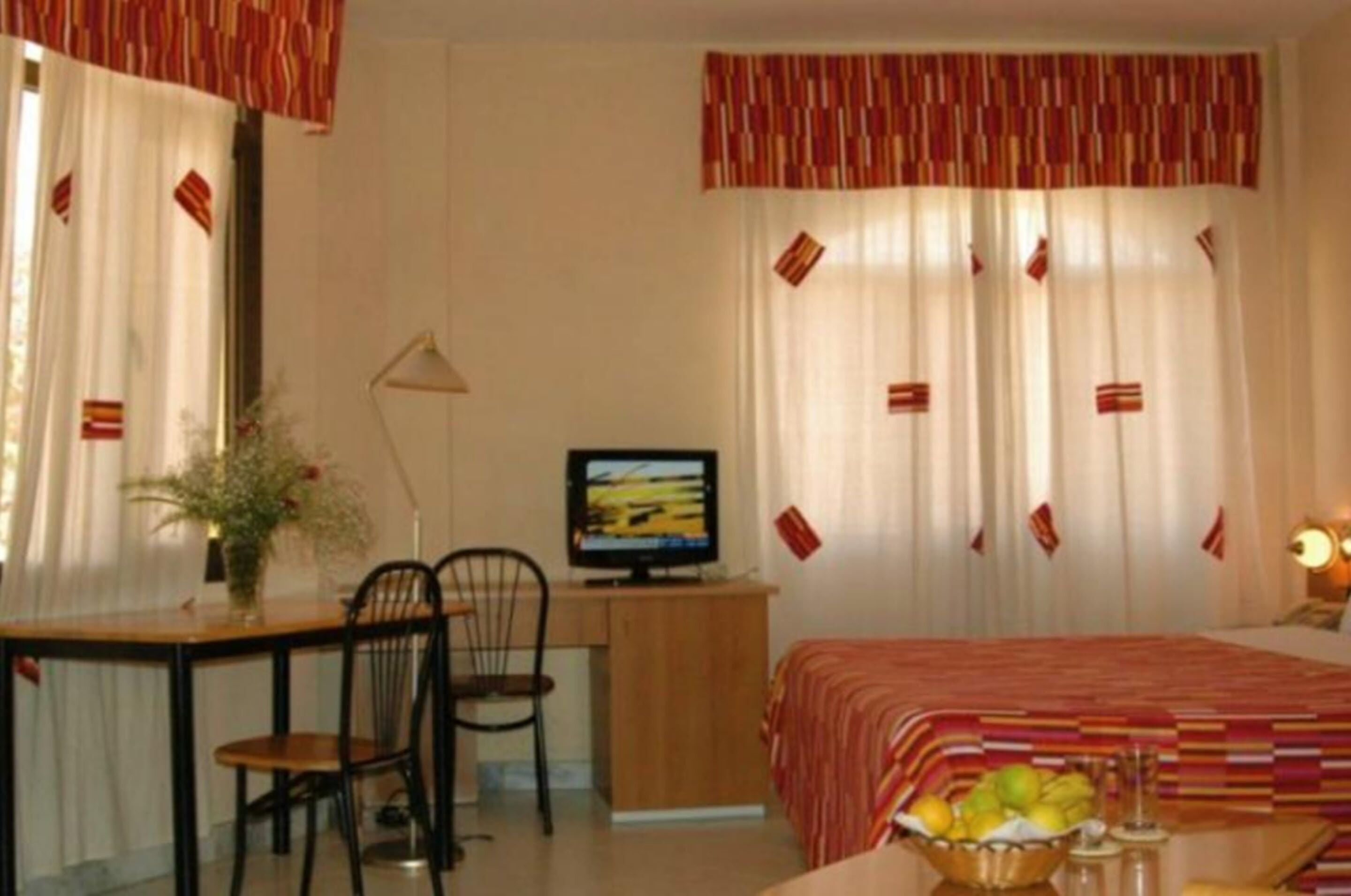 A hotel room with a bed, a desk with a computer, a chair, and a table with a fruit bowl.
