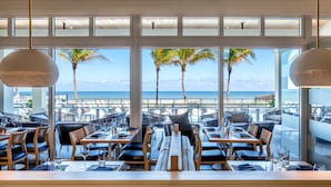 A restaurant with a view of the beach and palm trees. Tables are set with chairs and dining tables. - Hutchinson Shores Resort & Spa (Jensen Beach)