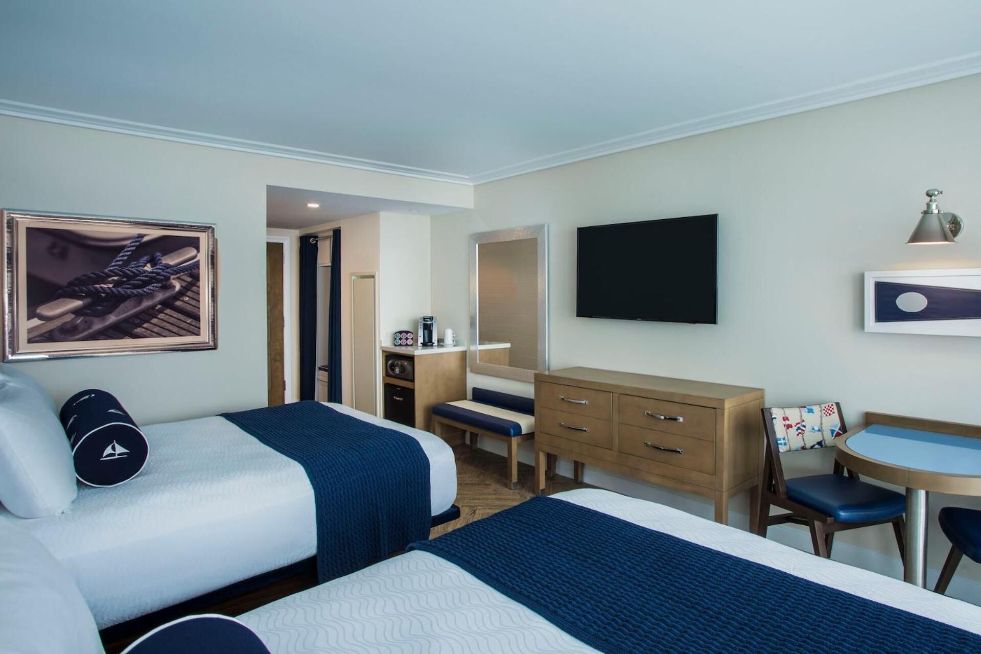 Quarto de hotel com duas camas, uma escrivaninha, uma cadeira, uma televisão e uma máquina de café.