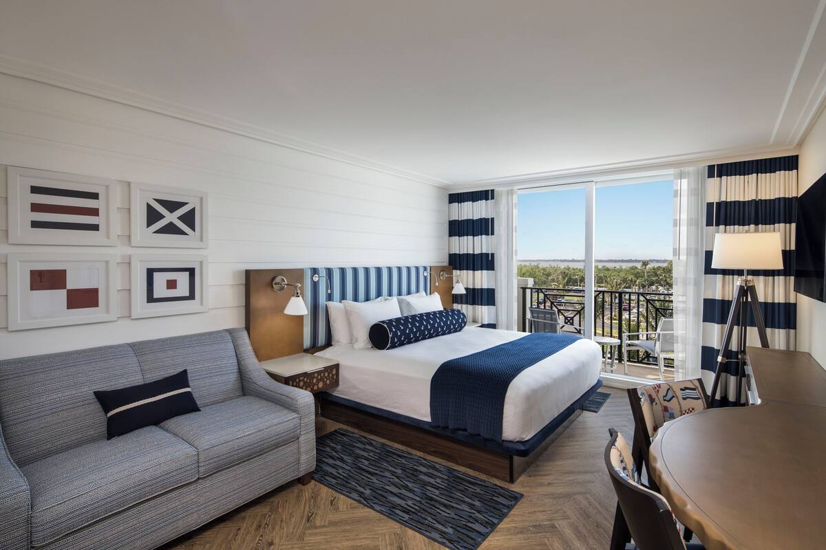 A hotel room with a bed, a sofa, a desk, and a balcony with a view.