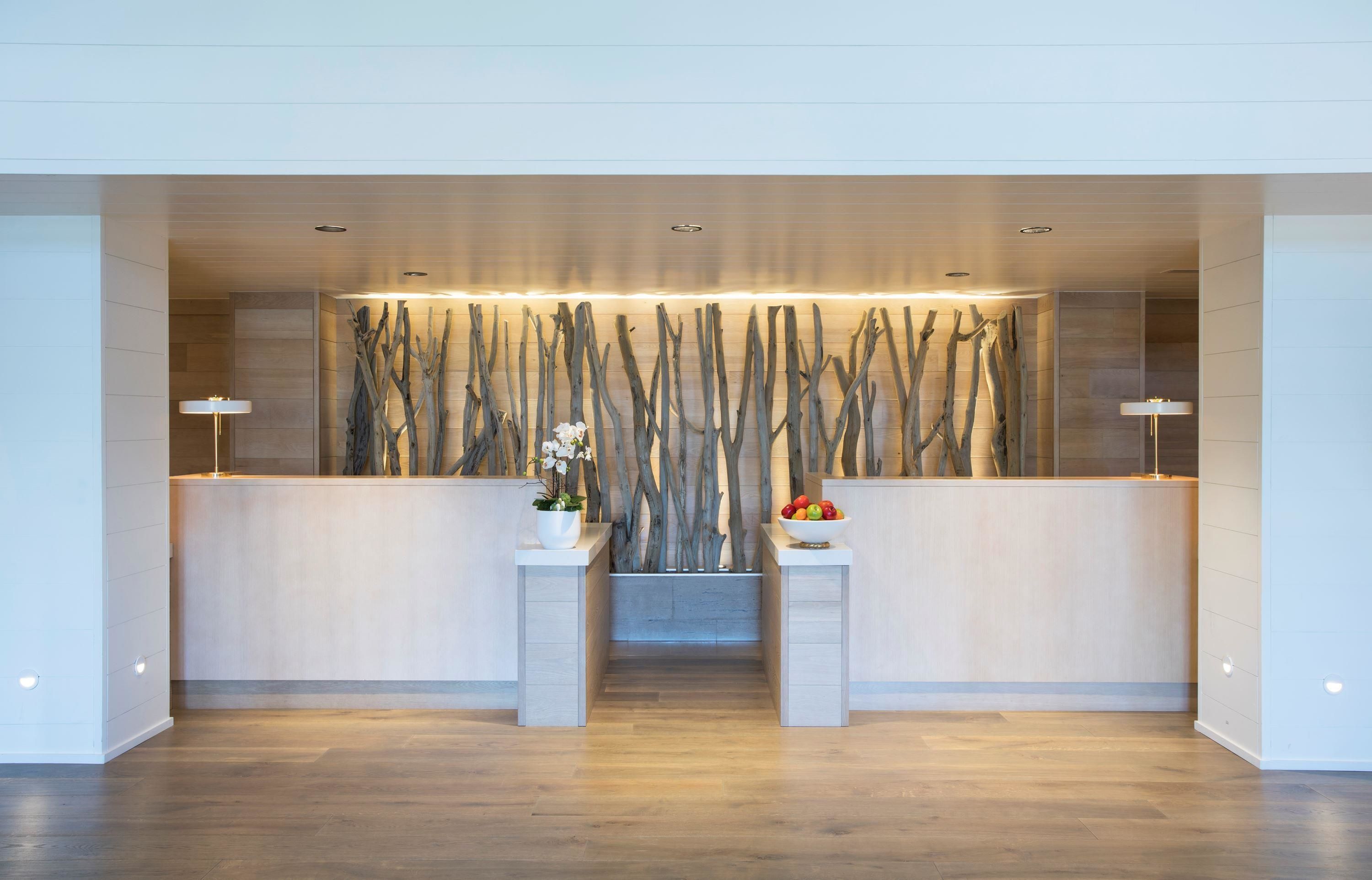 A reception area with a modern design, featuring a wooden reception desk, a wall-mounted light fixture, and a small plant on the desk.