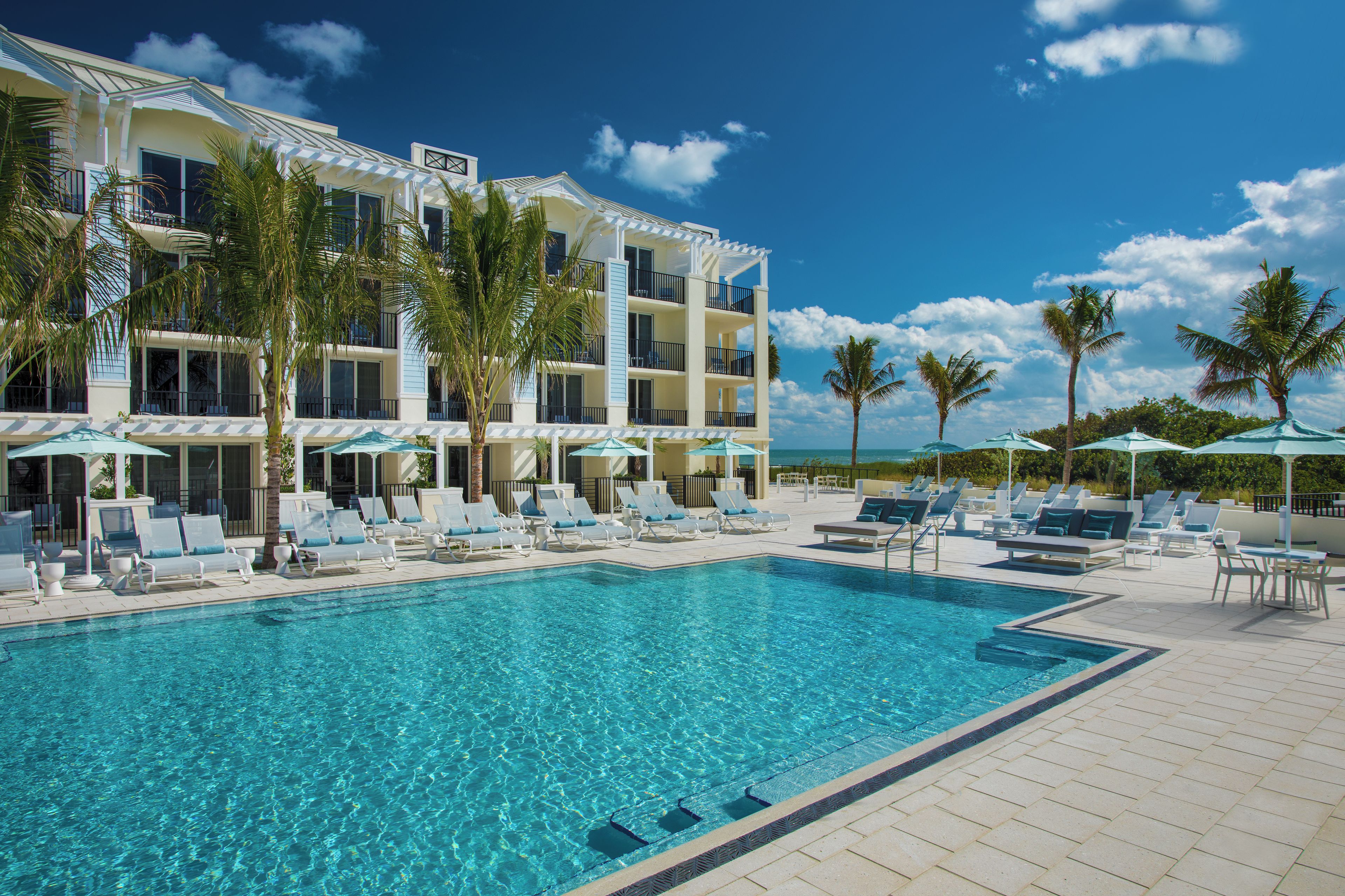 Un hôtel doté d’une piscine, de chaises longues et de palmiers.