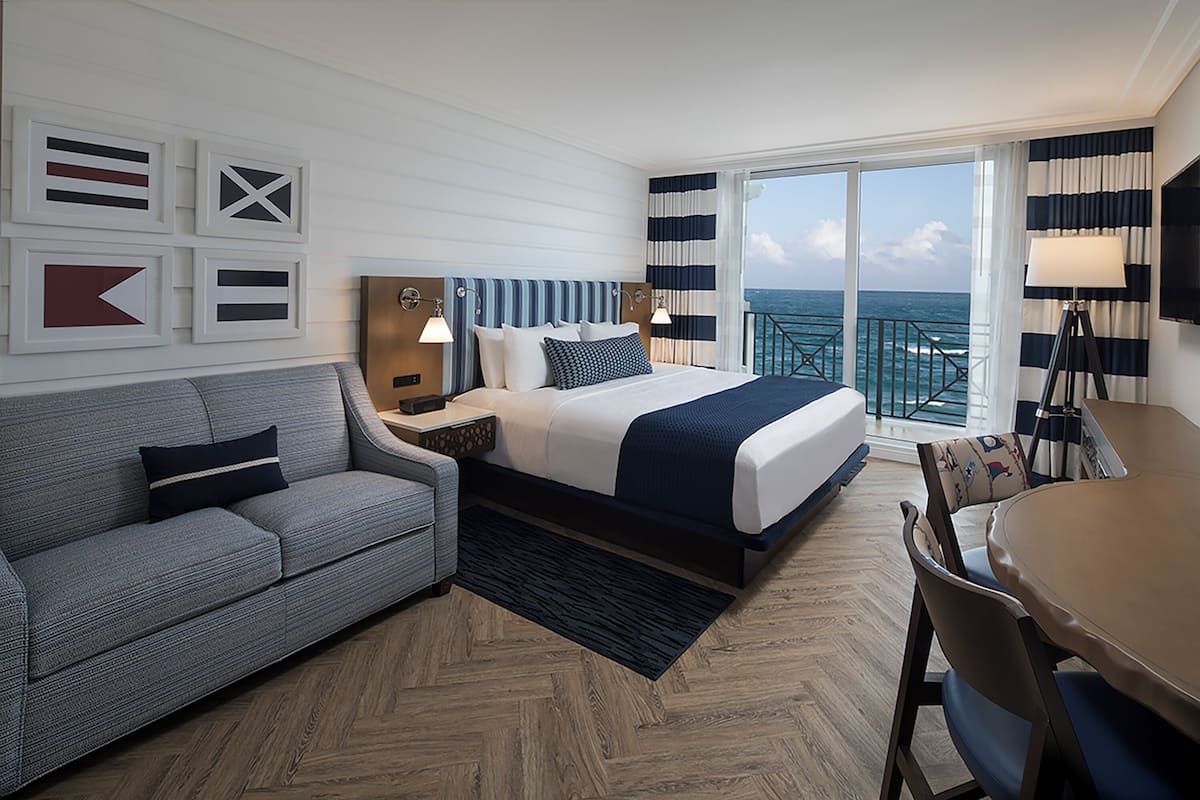 A hotel room with a bed, a sofa, a desk, and a view of the ocean.