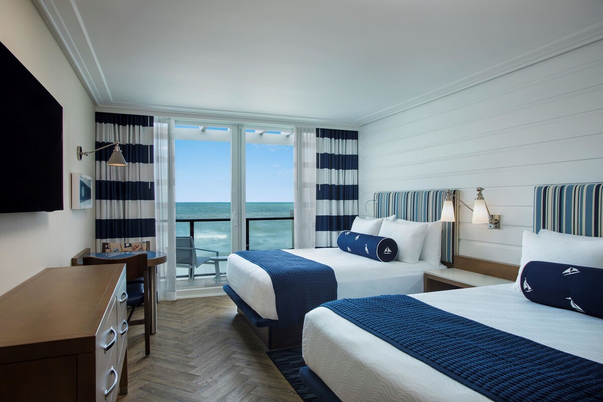 Una habitación de hotel con dos camas, un escritorio y vista al océano.