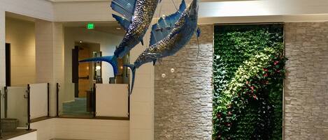 A spacious lobby with a high ceiling, a large glass sculpture, a stone wall with greenery, and modern seating areas.