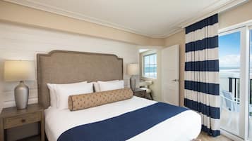 Habitación de hotel con una cama grande, una mesita de noche, una lámpara y vista al océano a través de un ventanal corredero.