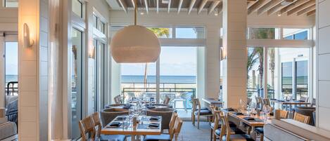 A restaurant with tables set for dining, large windows, and a view of the ocean.