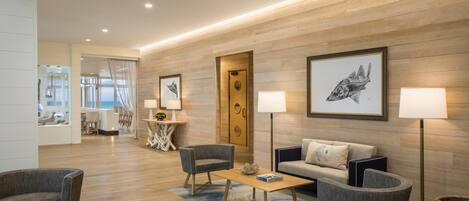 Un vestíbulo de hotel moderno con una pared de madera, un sofá, dos sillones, una mesa de centro y obras de arte enmarcadas.