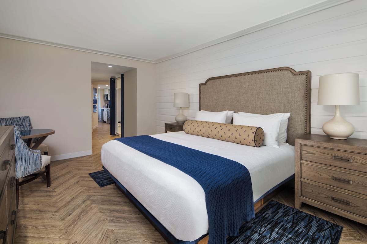 A hotel room with a large bed, a desk, a chair, and a nightstand with lamps.